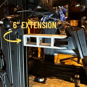 May include: A 6-inch extension for a 3D printer, featuring a gray, 3D-printed arm with three slots and a black, rectangular mount. The extension is attached to a black metal frame.