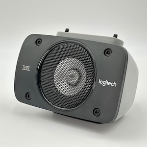 Op de afbeelding: Een zwarte Logitech-luidspreker met een rond luidsprekerrooster en de tekst "THX" en "logitech" gedrukt op de voorkant.