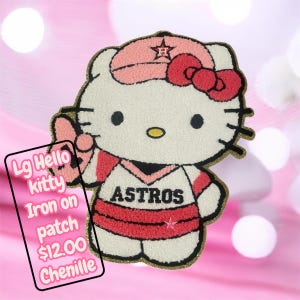 Może przedstawiać: Duża, naszywana aplikacja z chenille przedstawiająca Hello Kitty w baseballowym mundurze Astros. Aplikacja jest biała, różowa, czerwona i czarna ze złotym obramowaniem. Tekst "ASTROS" znajduje się na piersi. Aplikacja jest na różowym tle.