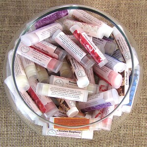 May include: A glass bowl filled with various flavored lip balms in tubes. The lip balm flavors include Strawberry Glaze, Cookie Dough, Vanilla-Vanilla, Chocolate Raspberry, and Butter.