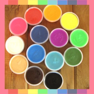 May include: A collection of 12 small bowls filled with different colored play dough. The bowls are arranged in a circle on a wooden surface. The colors include red, orange, yellow, green, blue, purple, pink, brown, white, and black.