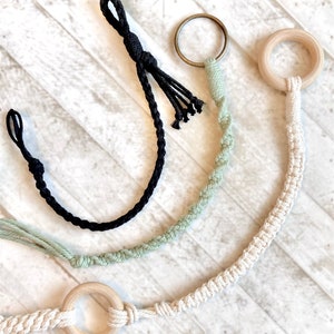 May include: Three macrame plant hangers with wooden rings. One is black, one is green, and one is natural white.