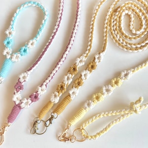 Puede incluir: Tres cordones de macramé con detalles de flores. Los cordones son de color rosa, azul y amarillo. Cada cordón tiene un anillo de metal dorado en un extremo.