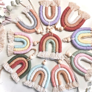 May include: A collection of 10 colorful rainbow wall hangings with fringe details. Each rainbow is made of yarn and has a wooden bead at the end of the string.