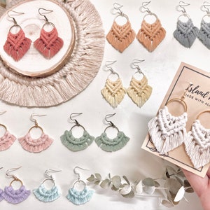May include: Assortment of handmade macrame earrings in various colors, including pink, purple, blue, green, white, and beige. The earrings are displayed on a white background with greenery and a sign that reads "Island Rm Made with Aloha".
