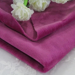 May include: A close-up of a folded piece of soft, plush fabric in a deep purple color. The fabric has a velvety texture and is perfect for crafting projects or making cozy garments.