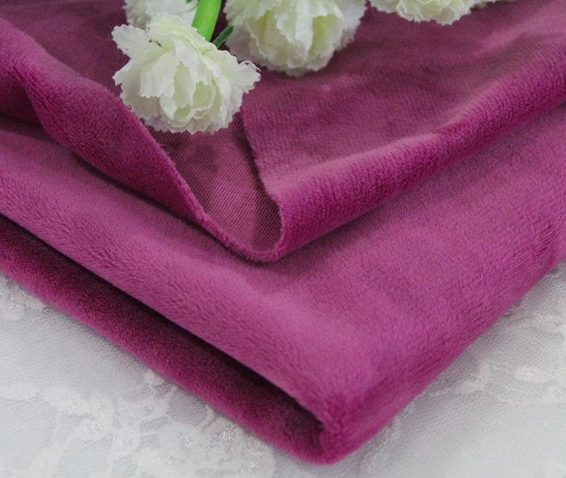 May include: A close-up of a folded piece of soft, plush fabric in a deep purple color. The fabric has a velvety texture and is perfect for crafting projects or making cozy garments.