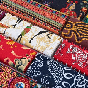 May include: An assortment of folded fabric pieces featuring diverse patterns and colours. Designs include floral, geometric, and cultural motifs. Colours range from red and blue to yellow and white, showcasing a variety of textile patterns.