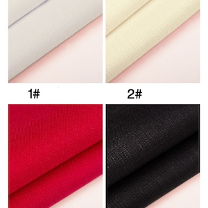 May include: Four fabric swatches in different colors: white, cream, red, and black. The swatches are folded in half and placed on a pink surface.