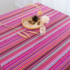 May include: A colorful striped tablecloth with pink, purple, red, and blue stripes. The tablecloth is made of cotton and has a woven texture. It is perfect for adding a touch of color and style to any dining table.