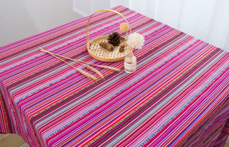 May include: A colorful striped tablecloth with pink, purple, red, and blue stripes. The tablecloth is made of cotton and has a woven texture. It is perfect for adding a touch of color and style to any dining table.
