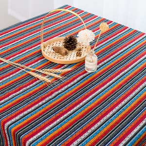 May include: A colorful striped tablecloth with a woven pattern. The tablecloth is red, orange, blue, and black. It is made of cotton and is perfect for a picnic or outdoor dining.