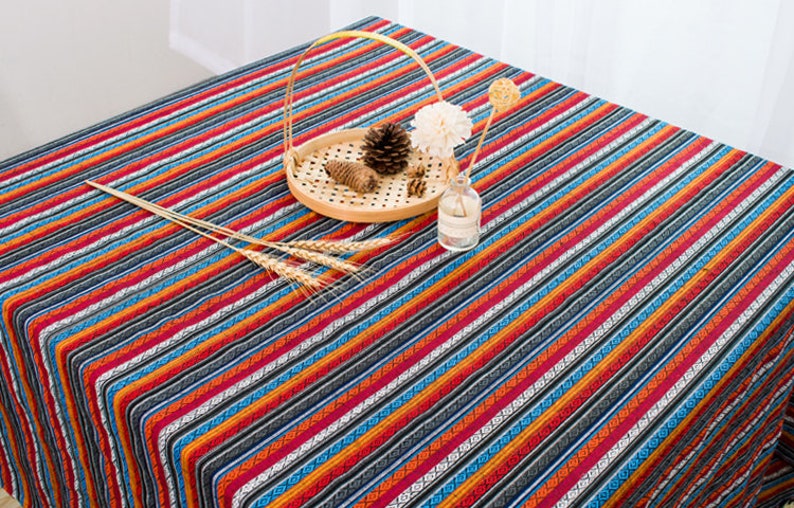 May include: A colorful striped tablecloth with a woven pattern. The tablecloth is red, orange, blue, and black. It is made of cotton and is perfect for a picnic or outdoor dining.