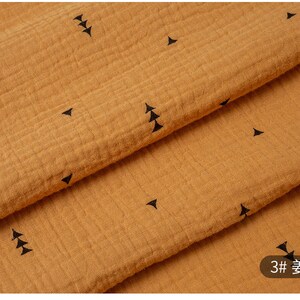 May include: A close-up of a mustard yellow fabric with a subtle texture and a repeating pattern of small black triangles. The fabric is folded in half, showing the pattern on both sides. The text "3#  麦黄" is visible in the lower right corner of the image.