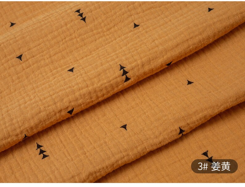 May include: A close-up of a mustard yellow fabric with a subtle texture and a repeating pattern of small black triangles. The fabric is folded in half, showing the pattern on both sides. The text "3#  麦黄" is visible in the lower right corner of the image.