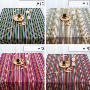 May include: Four different striped tablecloths with a woven texture. The tablecloths are in various colors, including blue, green, brown, beige, red, purple, orange, and yellow. Each tablecloth has a basket with a pine cone and a small vase with flowers on top.
