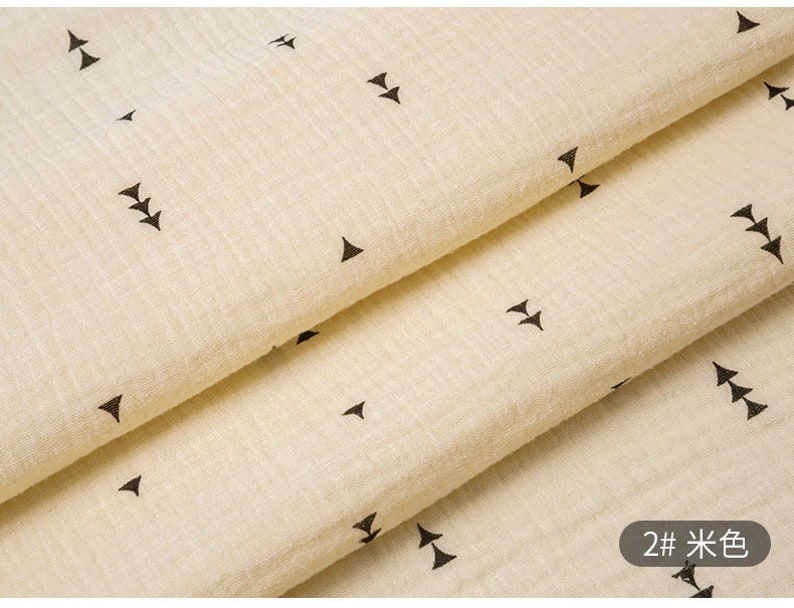 May include: Close-up of a beige fabric with a repeating pattern of black arrows. The fabric is folded in thirds, and the text "2# 米色" is visible in the bottom right corner.