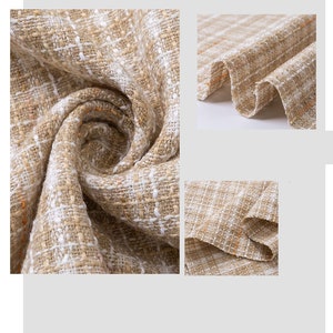 Op de afbeelding: Close-up van een geweven stof in beige en wit met een geruit patroon. De stof is zacht en textuurrijk, met een subtiele glans.