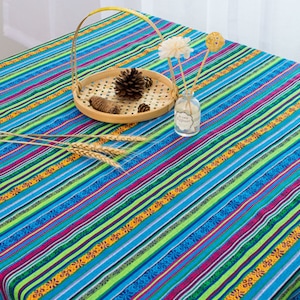 May include: A blue and green striped tablecloth with a colorful floral pattern. The tablecloth is decorated with a small wooden bowl filled with pine cones and a glass bottle with a flower.