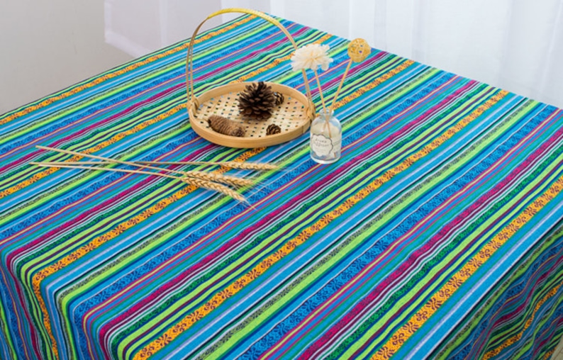 May include: A blue and green striped tablecloth with a colorful floral pattern. The tablecloth is decorated with a small wooden bowl filled with pine cones and a glass bottle with a flower.