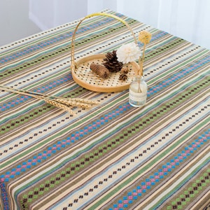 May include: A striped tablecloth with brown, green, blue, and white stripes. The tablecloth has a woven pattern and is made of cotton.