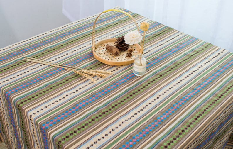 May include: A striped tablecloth with brown, green, blue, and white stripes. The tablecloth has a woven pattern and is made of cotton.