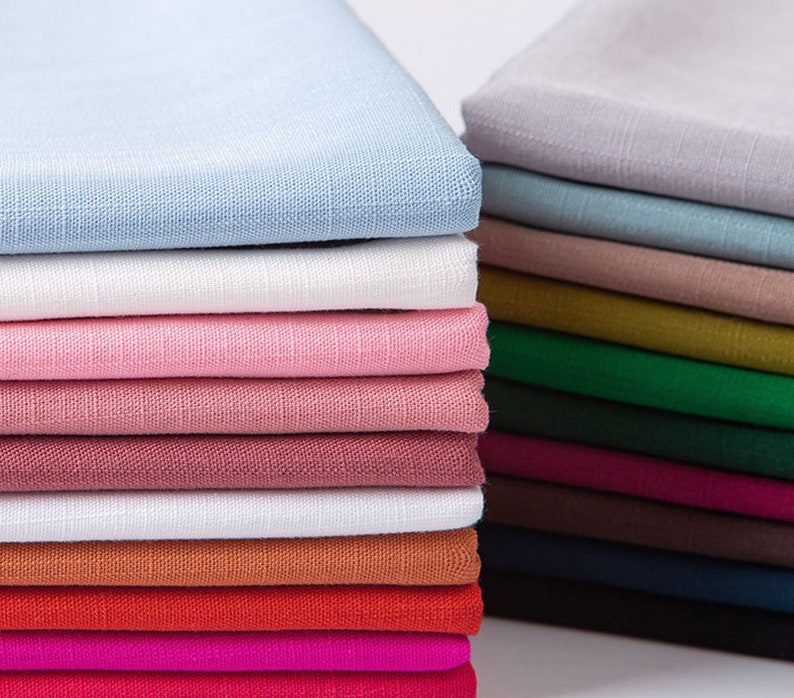 May include: Stacks of folded fabric in various colors, including light blue, white, pink, and red. The fabric appears to be linen or a similar woven material, with a slightly textured surface. The image showcases a range of hues, from pastels to deeper tones.