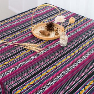May include: A black and pink striped tablecloth with a geometric pattern. The tablecloth is decorated with a wooden tray, a pine cone, and a glass vase with flowers.