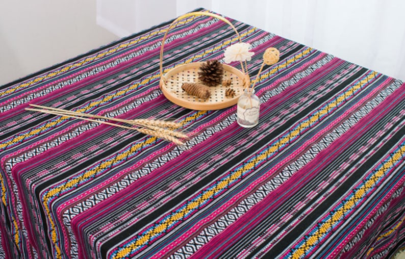 May include: A black and pink striped tablecloth with a geometric pattern. The tablecloth is decorated with a wooden tray, a pine cone, and a glass vase with flowers.