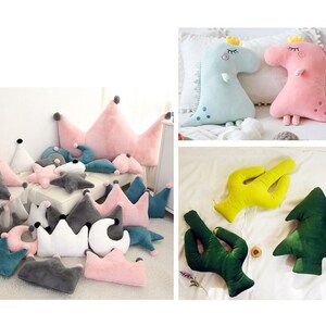 May include: A collection of plush pillows in various shapes and colors, including crowns, stars, moons, cacti, and a Christmas tree. The pillows are made of soft, fuzzy fabric and are perfect for adding a touch of whimsy to any room.