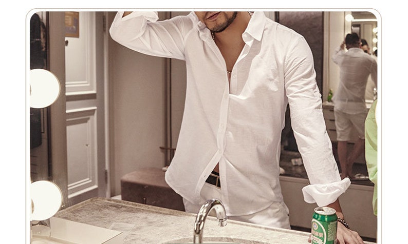 May include: A white linen shirt with long sleeves, partially unbuttoned, worn with white pants. The person is standing in front of a mirror, with a can of beer visible. The shirt has a classic collar and buttoned cuffs.