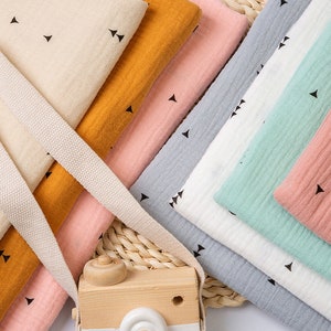 May include: A stack of fabric swatches in various colors, including beige, orange, pink, gray, white, and green. Each swatch features a small, repeating pattern of black triangles.
