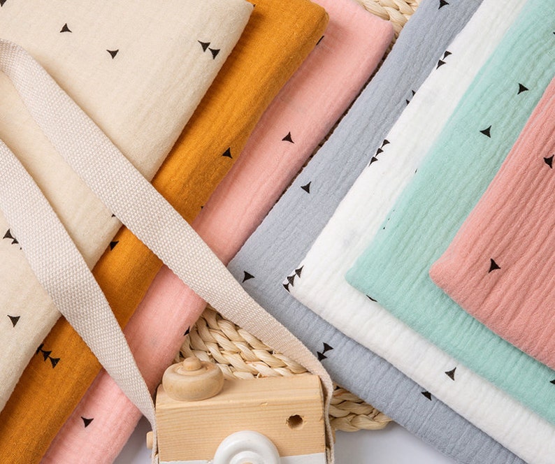May include: A stack of fabric swatches in various colors, including beige, orange, pink, gray, white, and green. Each swatch features a small, repeating pattern of black triangles.