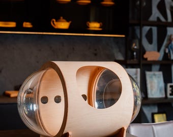 May include: A wooden cat bed with two clear plastic domes. The bed is light brown and has a rounded shape. It sits on four small legs.
