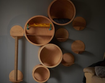 May include: A wall mounted cat tree made of wood with multiple circular shelves and a scratching post. The shelves are different sizes and are arranged in a random pattern. The scratching post is made of sisal rope and is attached to one of the shelves.