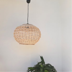 May include: A round, woven wicker pendant light fixture hangs from a black cord against a white wall.