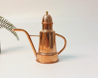 May include: A copper oil and vinegar dispenser with a spout and a lid. The dispenser has a traditional design and is perfect for adding a touch of elegance to any kitchen.