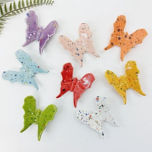 Puede incluir: Colección de figuras de mariposas de cerámica en varios colores, incluyendo morado, rosa, naranja, azul, rojo, amarillo, verde y blanco. Cada mariposa tiene un diseño moteado y está dispuesta sobre una superficie blanca.