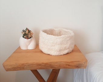 Può includere: Un vaso di ceramica bianca con fiori secchi si trova su un tavolo di legno accanto a un cesto bianco e soffice. Il tavolo è accanto a un letto bianco con un cuscino bianco.