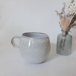Può includere: Una tazza in ceramica bianca con una glassa macchiata e una forma arrotondata. La tazza ha un manico ed è perfetta per gustare una bevanda calda.