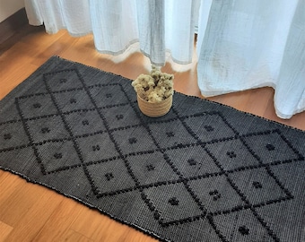 Puede incluir: Alfombra geométrica de patrón negro y blanco con textura en relieve. La alfombra está hecha de un material tejido y tiene un patrón de diamante.