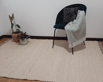 May include: A beige woven rug with a green velvet chair with a light blue throw blanket draped over the back. The chair has a black cushion with a black and white patterned design.