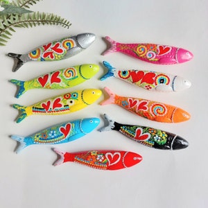 Op de afbeelding: Tien handgeschilderde houten visfiguren in verschillende kleuren, waaronder rood, geel, blauw, groen en roze. Elke vis heeft een uniek ontwerp met harten en swirls. De vissen zijn allemaal in dezelfde richting gericht en zijn in een rij gerangschikt.