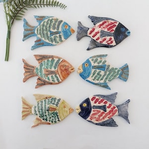 May include: Six ceramic fish wall decor in various colors and patterns. The fish are all different sizes and shapes, with some having a more realistic look and others being more stylized. They are all painted in bright colors and have a glossy finish.