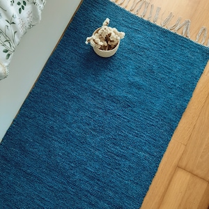 Pode incluir: Um tapete azul turquesa com uma borda de franjas. O tapete é feito de um material macio e texturizado e tem um brilho sutil.