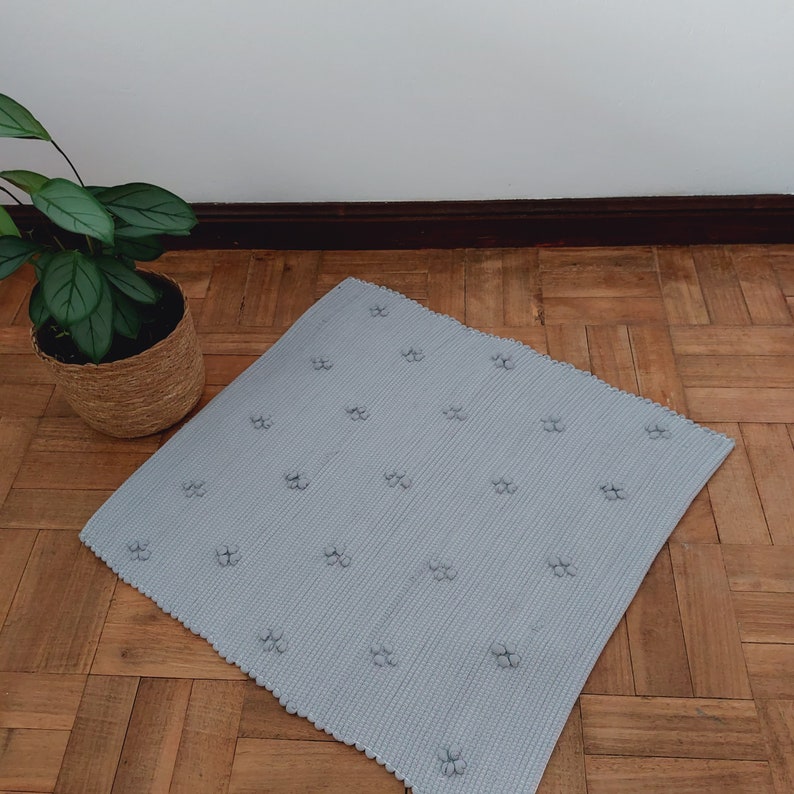 Puede incluir: Una alfombra de ba&ntilde;o gris claro con una superficie texturizada y un patr&oacute;n repetitivo de peque&ntilde;as flores en relieve.