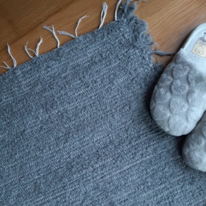May include: A gray, fuzzy rug with a fringe border. Two fuzzy gray slippers are on the rug.