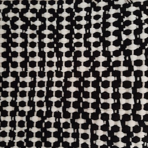 May include: Black and white woven fabric with a geometric pattern. The fabric has a textured surface and a slightly raised design.