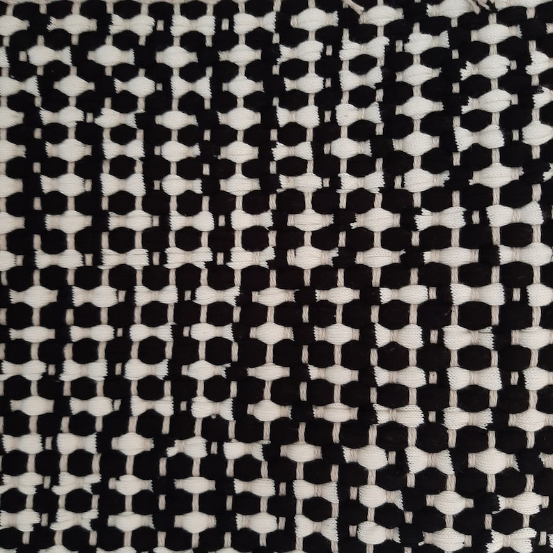 May include: Black and white woven fabric with a geometric pattern. The fabric has a textured surface and a slightly raised design.