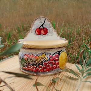 May include: A ceramic wall mounted salt and pepper shaker with a wooden lid. The shaker is decorated with a hand-painted design of cherries, leaves, and berries.